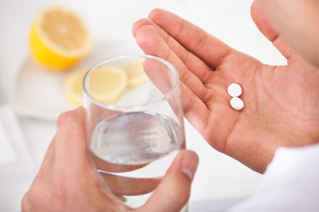 hands holding glass of water and two pills